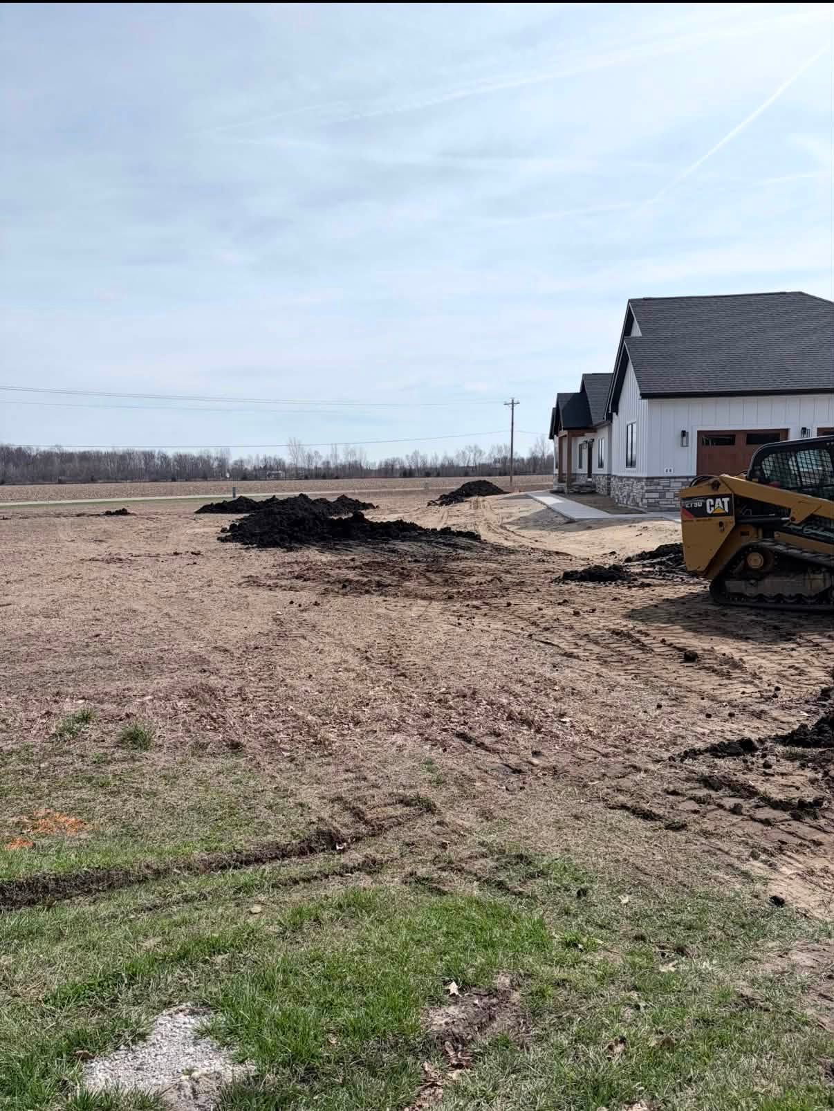 Site grading with material piles and a tracked skid steer